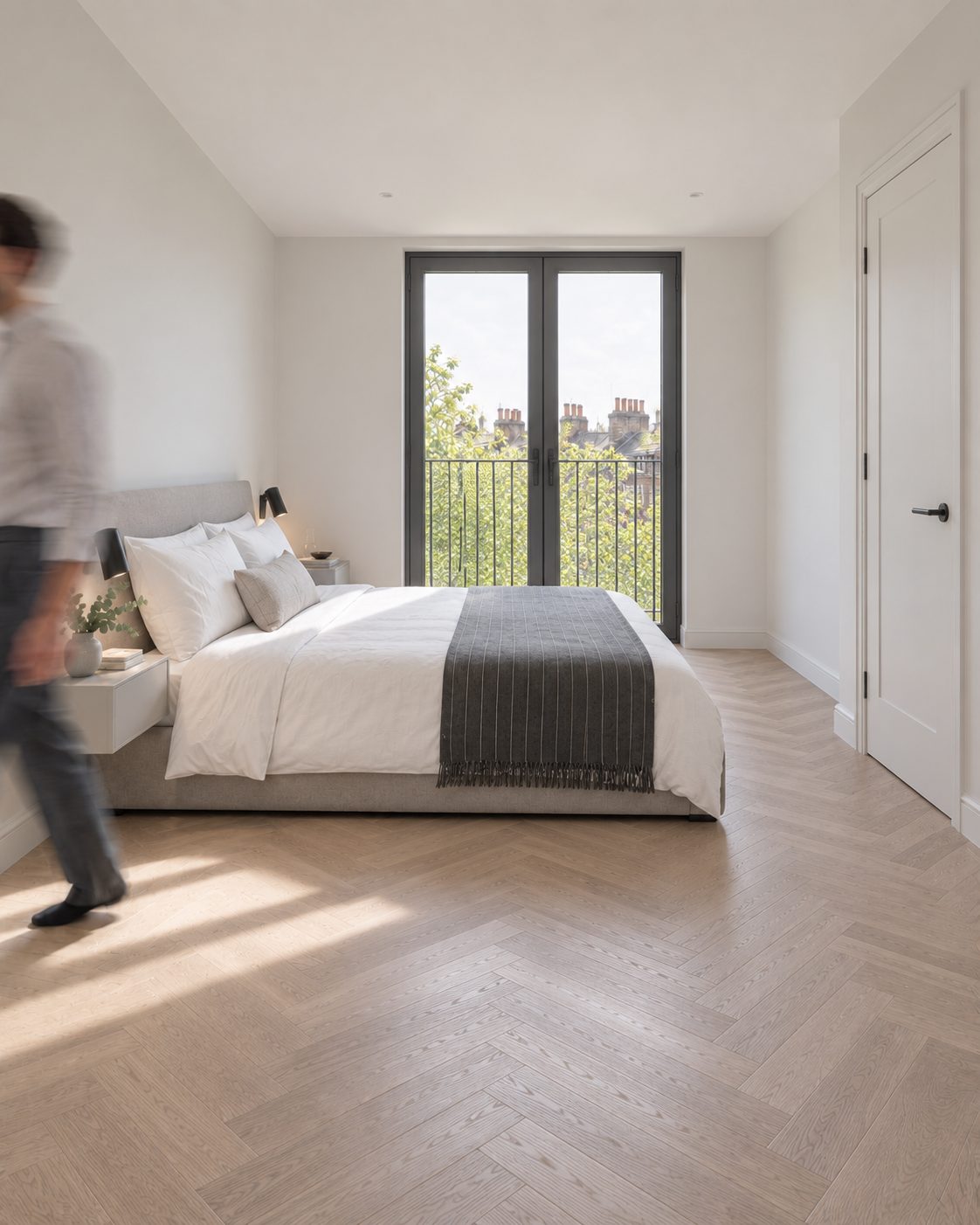 Bright bedroom in a new home with a herringbone oak floor and French doors to a Juliet balcony over London rooftops